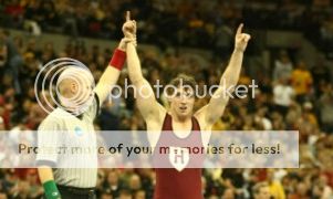 A picture of JP O'Connor from Harvard getting his hand raised after winning the NCAA wrestling championship.
